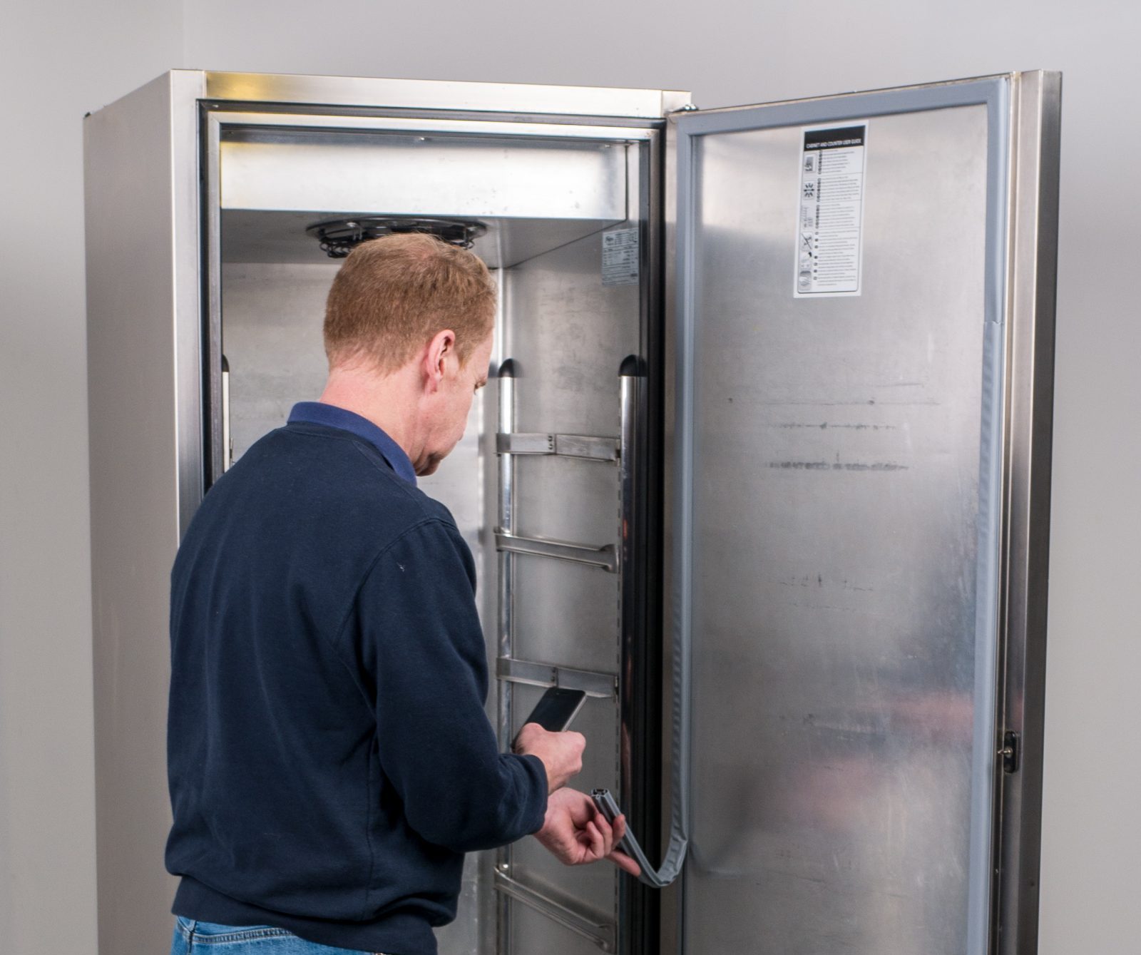 Man changing fridge seals in a commercial kitchen