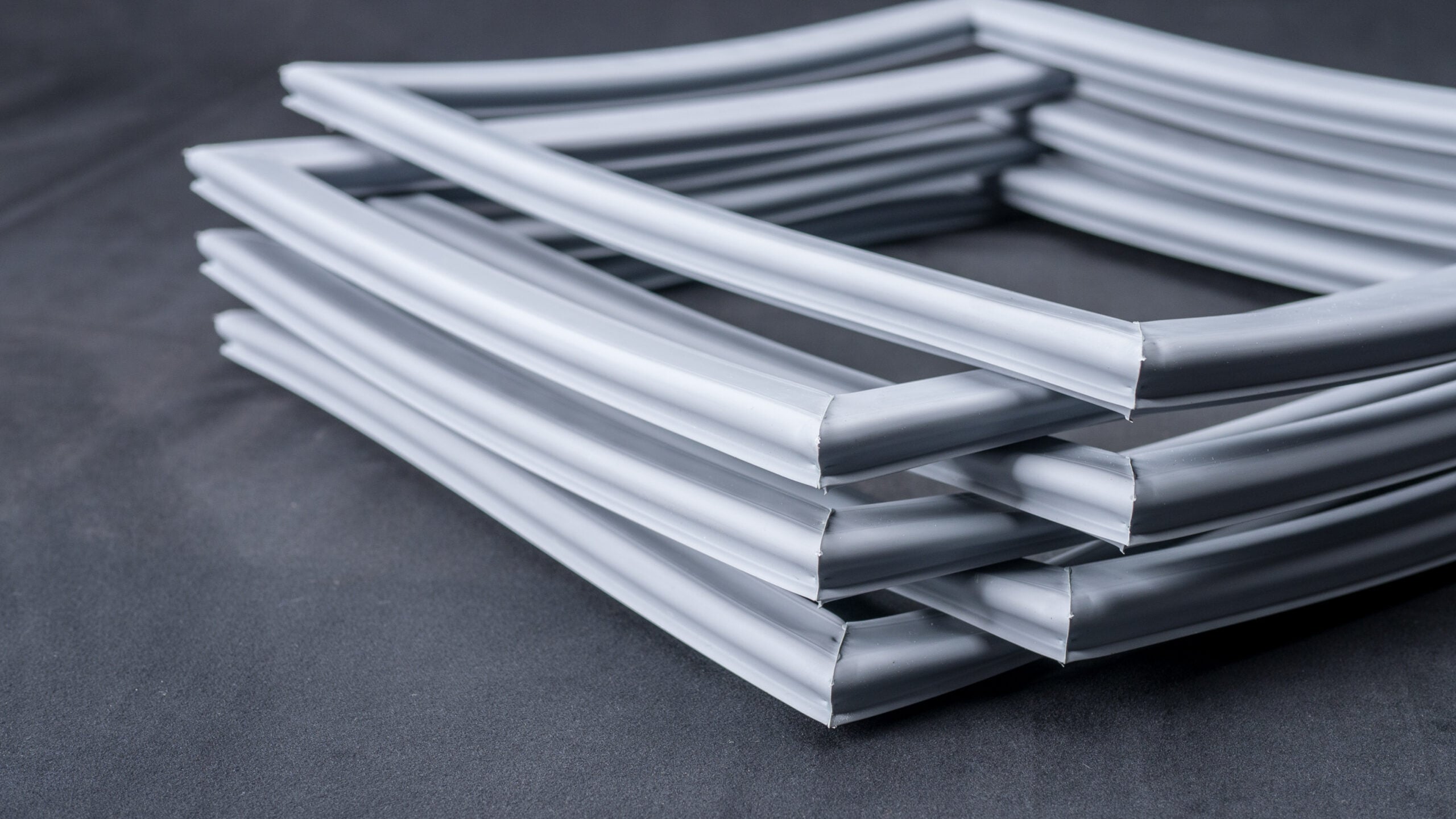 Easy and value for money! 1 A stack of grey rubber draught excluders, arranged in a neat, square shape on a dark surface. The flexible strips have a hollow centre and smooth texture, suggesting they are used for sealing gaps in windows or doors to prevent draughts.