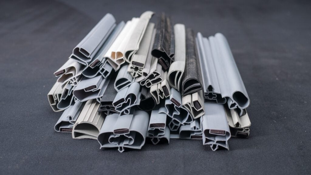 A pile of various grey and black rubber or plastic weatherstripping seals, neatly arranged on a dark surface, showing different shapes and cross-sections, likely used for doors or windows to prevent draughts and water leakage.