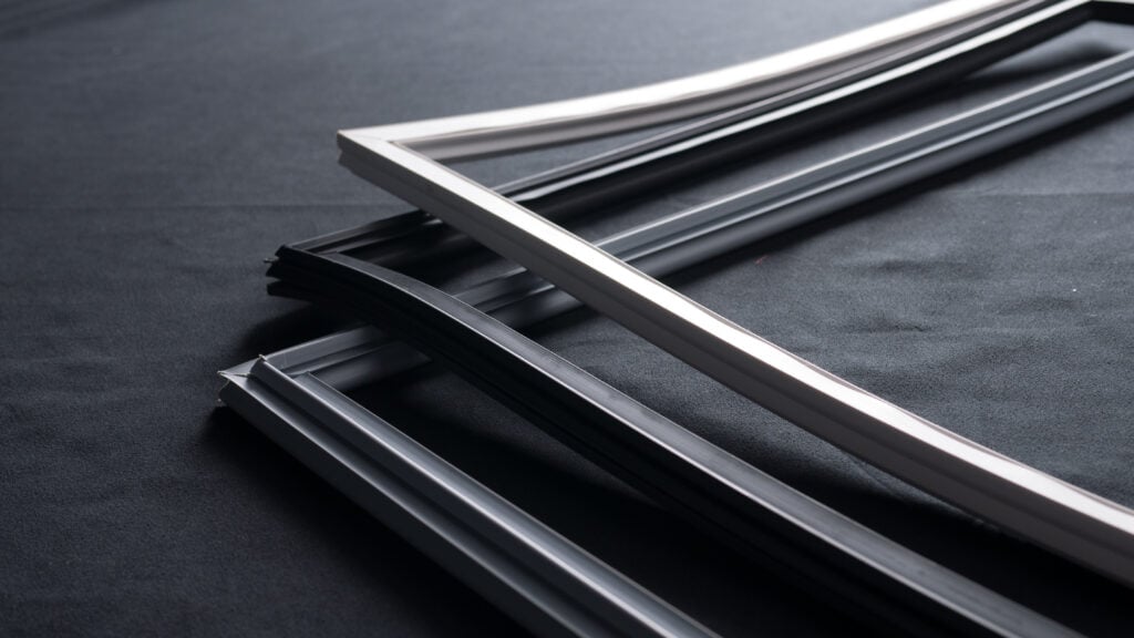 Several empty, overlapping rectangular picture frames, mostly black with one white frame, are placed on a black surface. The frames are positioned at an angle, creating strong shadows and a minimalist, modern composition.