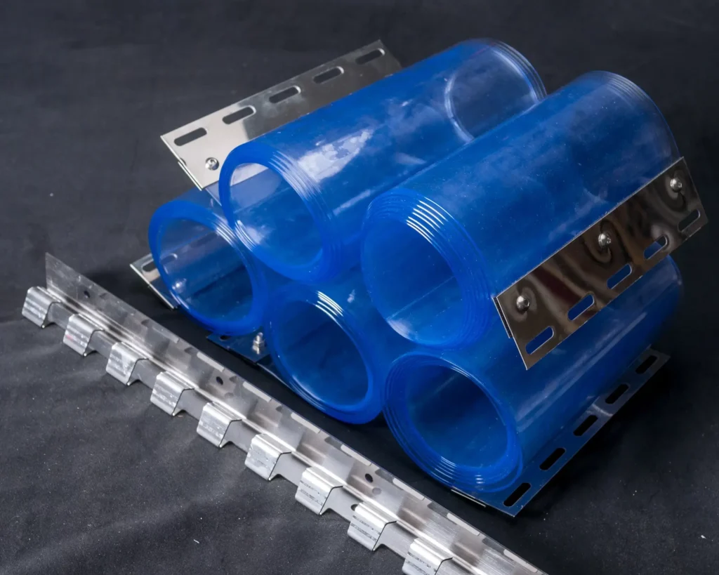 Six transparent blue plastic cylinders are arranged in two rows and held together by metal brackets with multiple holes. Another segmented metal strip lies in front on a dark surface, suggesting an industrial or assembly application.