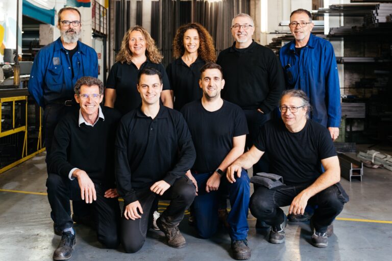 Group of smiling colleagues wearing formal clothes and looking at camera in garage in modern industrial factory workshop with various equipment for work