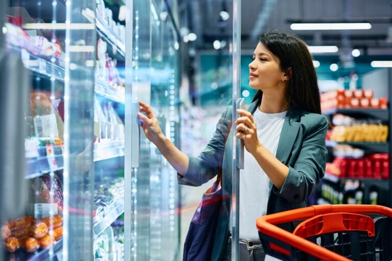 Smiling woman taking groceries from refrigerator while shopping in supermarket. Copy space.